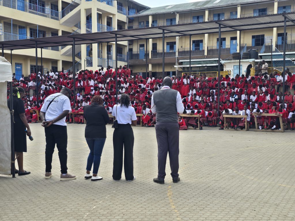 The team standing before a large school assembly